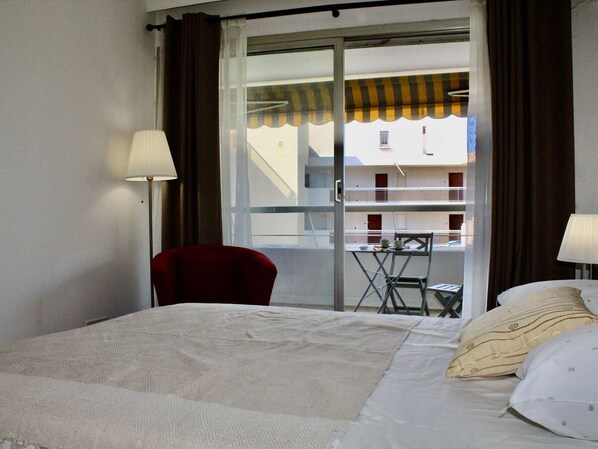 Een hotelkamer met een bed, een rode stoel, een tafeltje met een kopje en uitzicht op een gebouw door een glazen deur.
