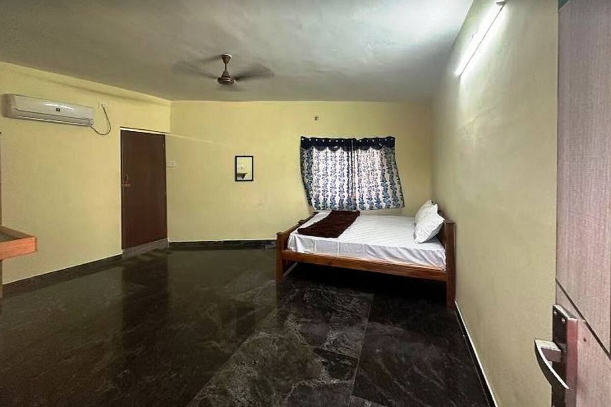 A room with a bed, a ceiling fan, an air conditioning unit, and a door.