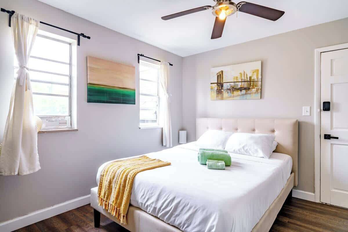 A bedroom with a bed, a ceiling fan, a painting, and a door.