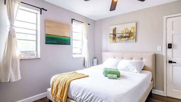 A bedroom with a bed, a ceiling fan, a painting, and a door.