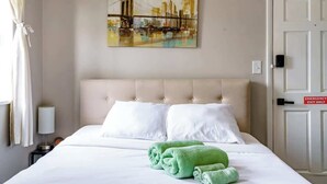 Camera d'albergo con un letto, cuscini bianchi, un asciugamano verde, un quadro di un ponte e un'uscita di sicurezza.