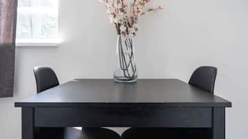 Une table à manger avec deux chaises noires, un vase avec des fleurs et une fenêtre avec des rideaux.