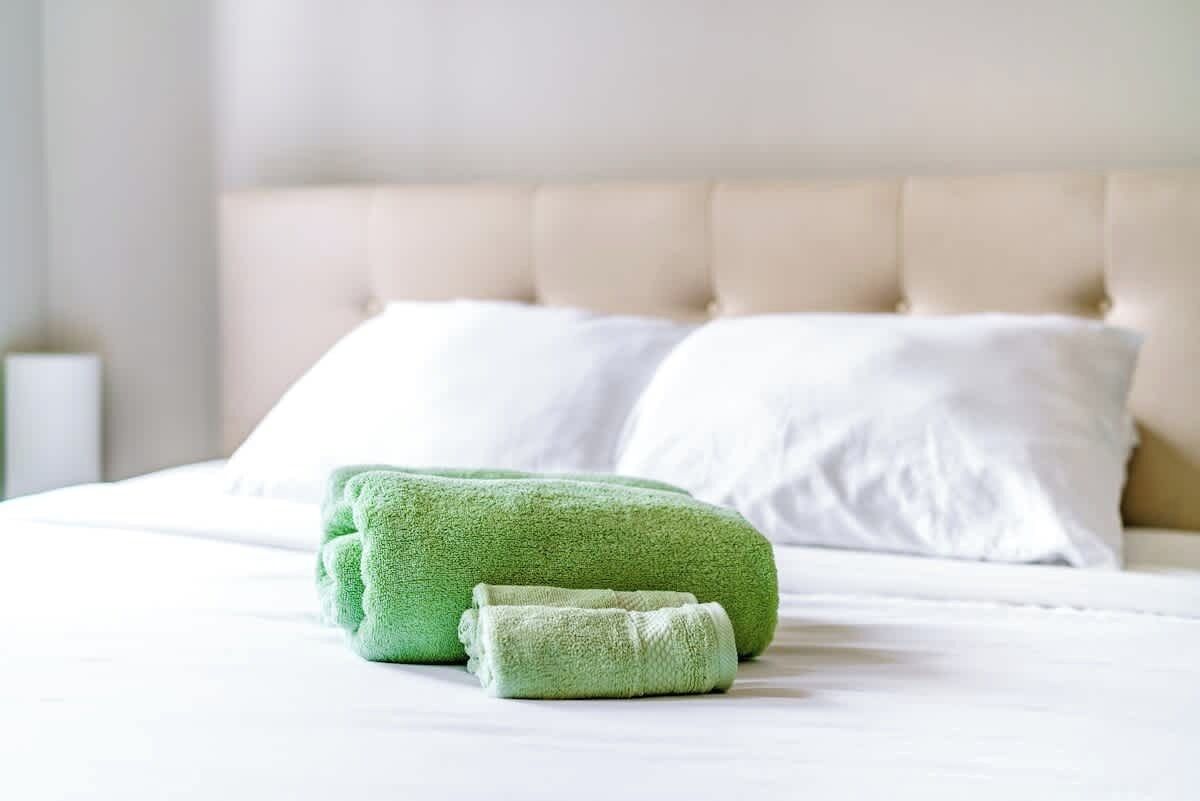 A neatly made bed with white linens and two green towels.