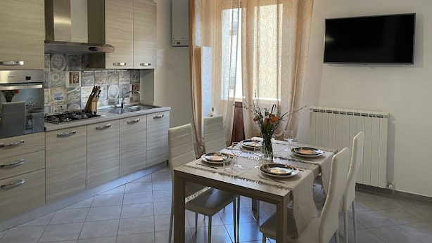 Une cuisine moderne avec un coin repas, un téléviseur à écran plat fixé au mur et une fenêtre avec des rideaux.