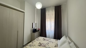 Une chambre à coucher avec un lit, une table de chevet avec une lampe, une armoire et une fenêtre avec des rideaux.