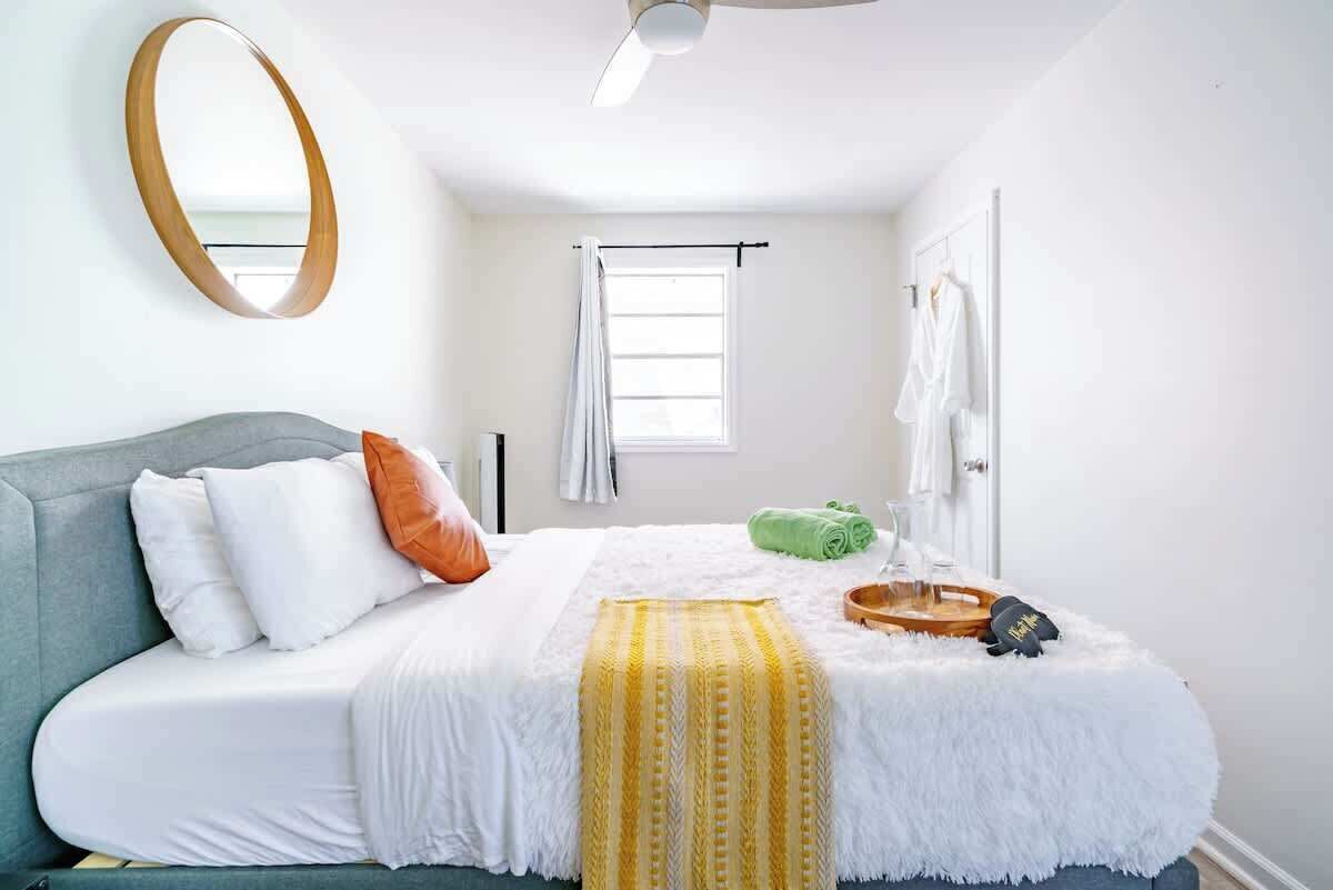 A bedroom with a bed, a mirror, a window, and a door.