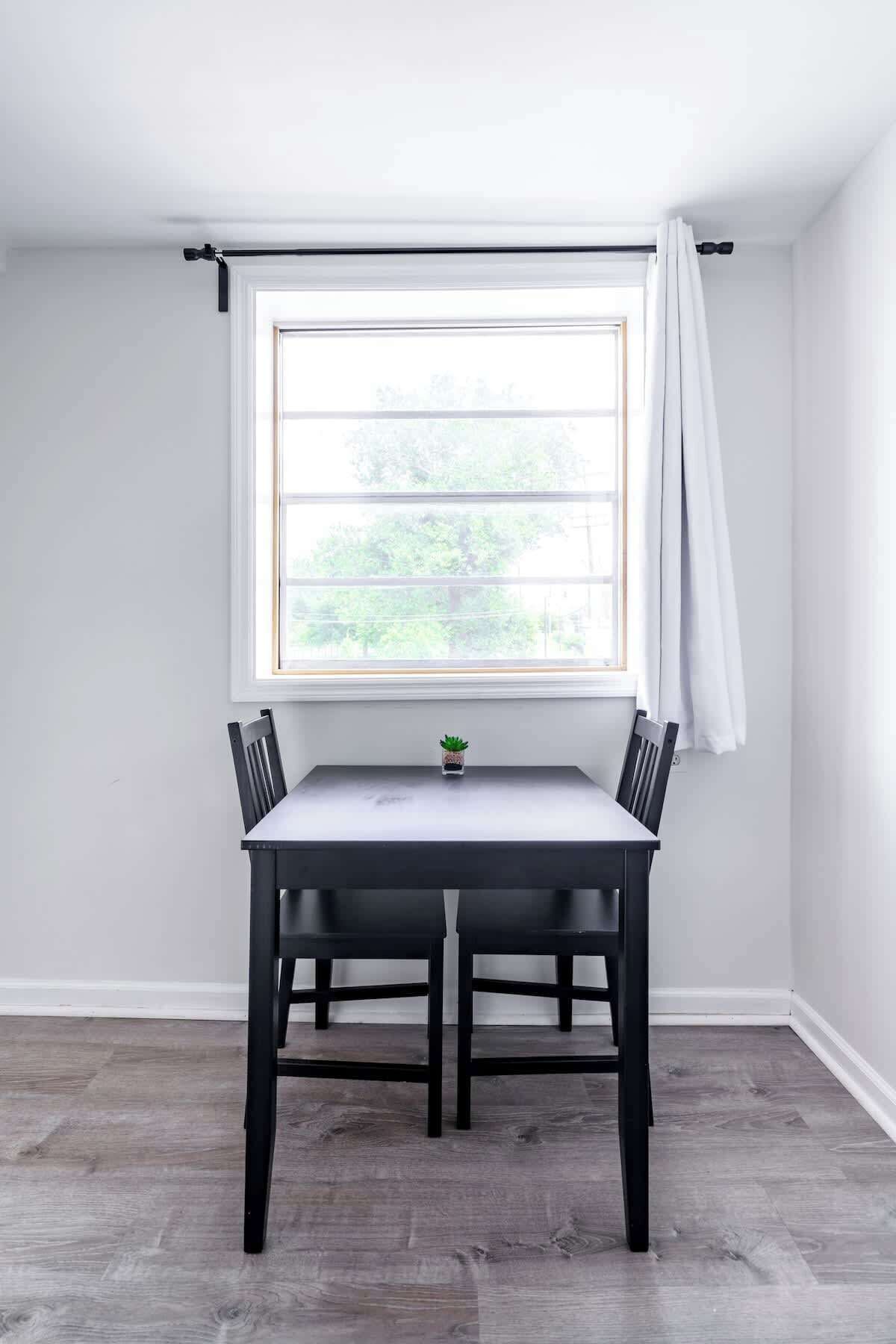 A dining area with a table and chairs, a window with a curtain, and a small plant on the windowsill.