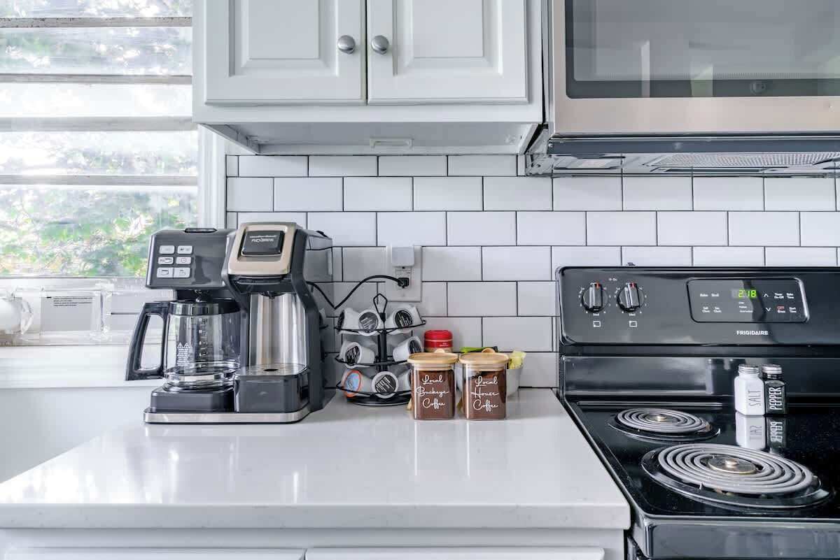 Uma cozinha com armários brancos, cafeteira, fogão e potes de especiarias com a etiqueta 'Café da Casa Especial'.