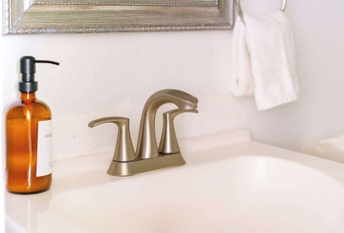 A bathroom with a white sink, a gold faucet, and a bottle of soap.