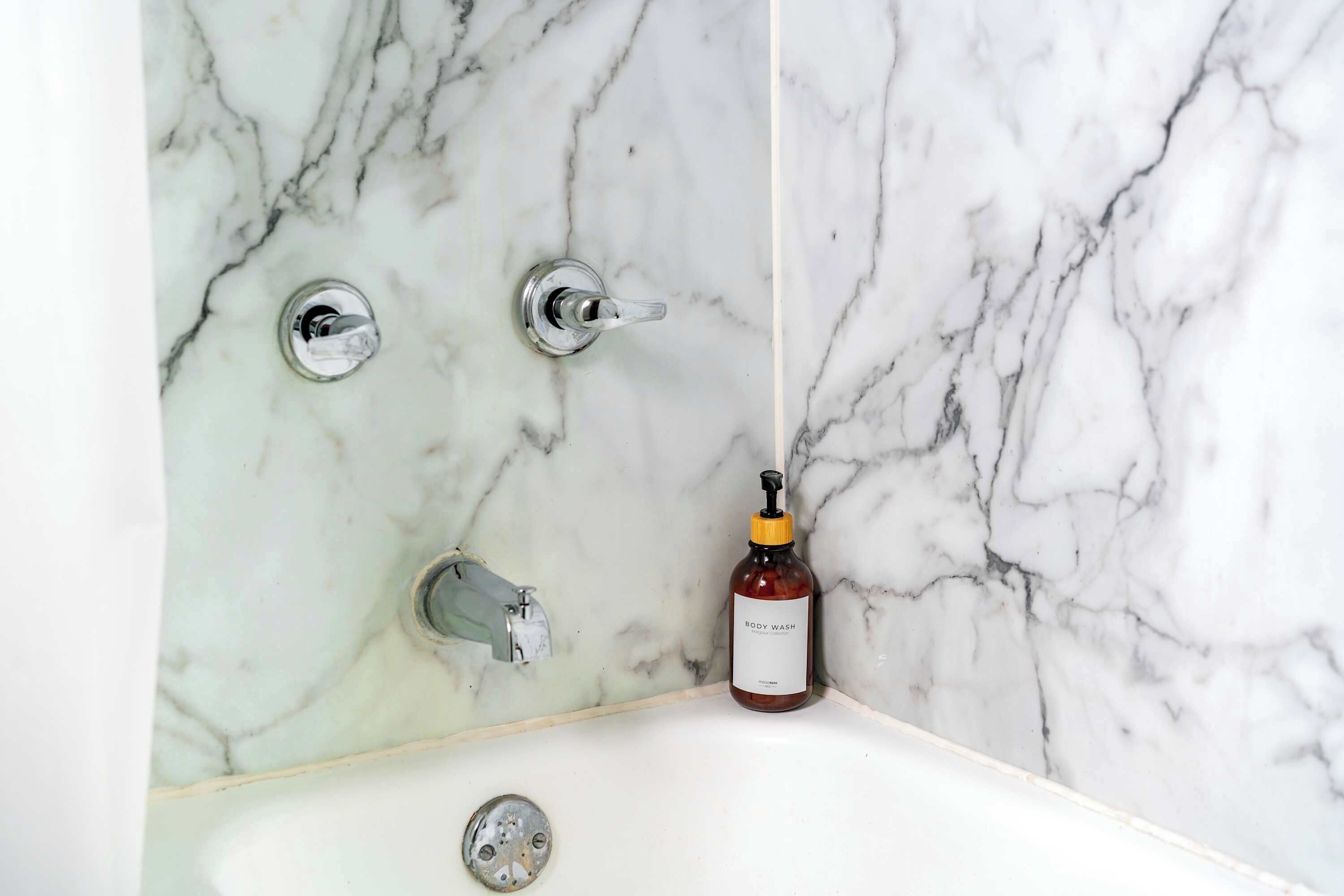 A bathroom with a marble wall, a bathtub, and a bottle of body wash.