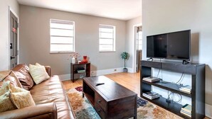 Ein modernes Wohnzimmer mit einer Ledersofa, einem Couchtisch, einem Fernseher auf einem Schrank und einem Bücherregal.