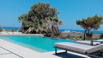 Una piscina con sillones de descanso y vistas al mar.