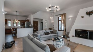 A spacious living area with a grey sofa, a round coffee table, and a fireplace. - Echo Villa (Santorini)