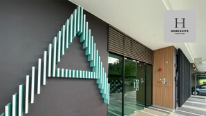 Een moderne entree van een gebouw met een opvallend geometrisch wandontwerp, een glazen deur en een houten paneelwand.