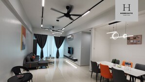 Een moderne woonkamer met een bank, eettafel en stoelen. Er is een plafondventilator, een televisie en een wandairconditioner.