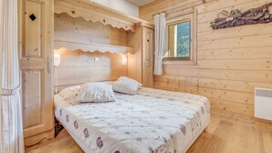 Une chambre confortable dans un chalet en bois, avec un lit, une fenêtre avec des rideaux et une étagère où sont rangées des chaussures.