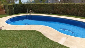 A swimming pool with a curved edge, surrounded by a well-maintained lawn and a hedge.