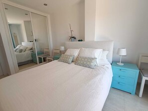 Quarto com cama grande, espelho, mesa de cabeceira com abajur e planta em vaso.