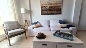 A modern living room with a white sofa, a wooden chair, a coffee table with decorative items, and a painting of birds on the wall.