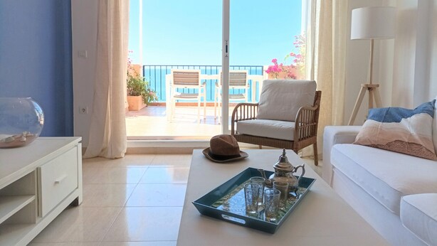 A bright room with a white sofa, a white table, and a balcony with a chair and potted plants.