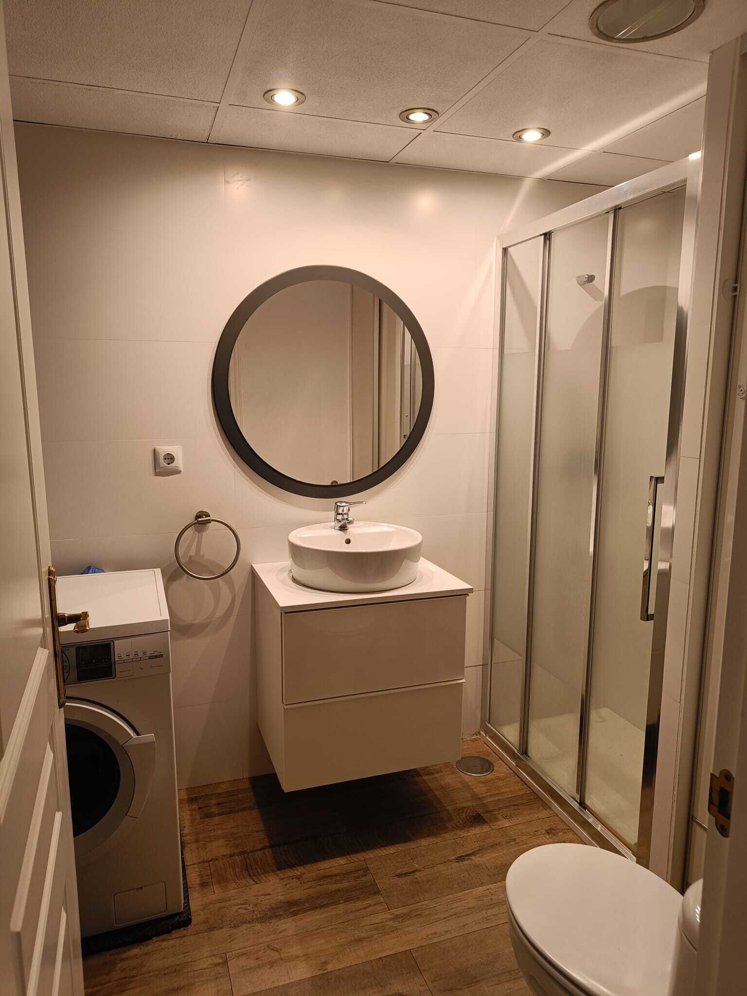 Un baño compacto con lavadora, lavabo con espejo e inodoro.