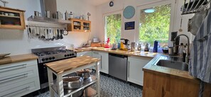 A kitchen with a stove, sink, and wooden countertop. There are cabinets, a clock, and a window with a view of trees.