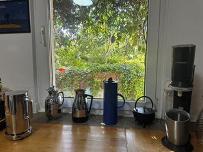 A kitchen with a window view of greenery, a coffee maker, a kettle, and a water dispenser.