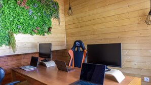 A wooden-paneled room with a long table, three laptops, two monitors, and a gaming chair.