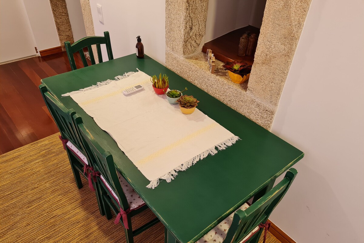 A green dining table with a white placemat, chairs with red bows, and potted plants.