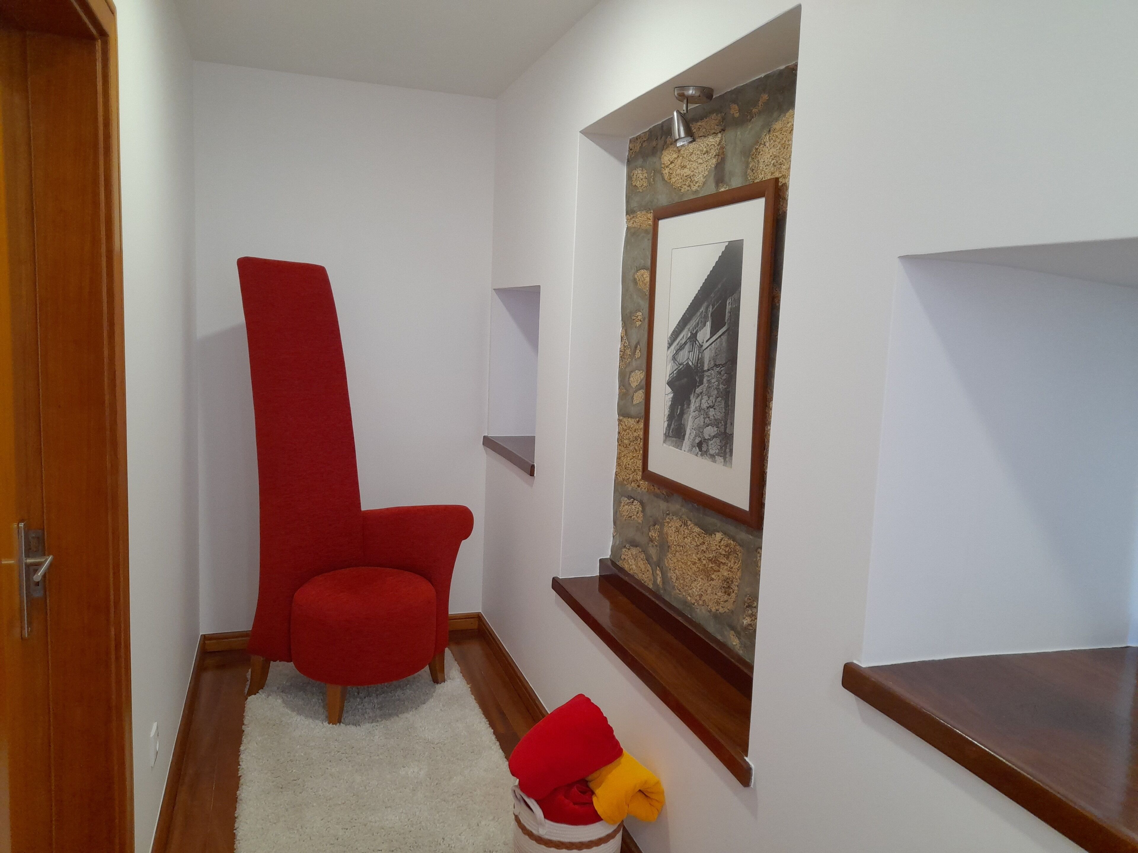 Una habitación con un sillón rojo, un tapete blanco, una puerta de madera y un cuadro enmarcado en la pared.