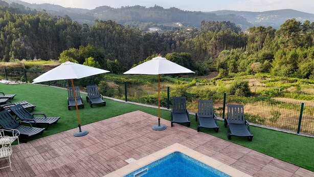 A pool area with lounge chairs and umbrellas, surrounded by a fence and a view of a forested landscape.