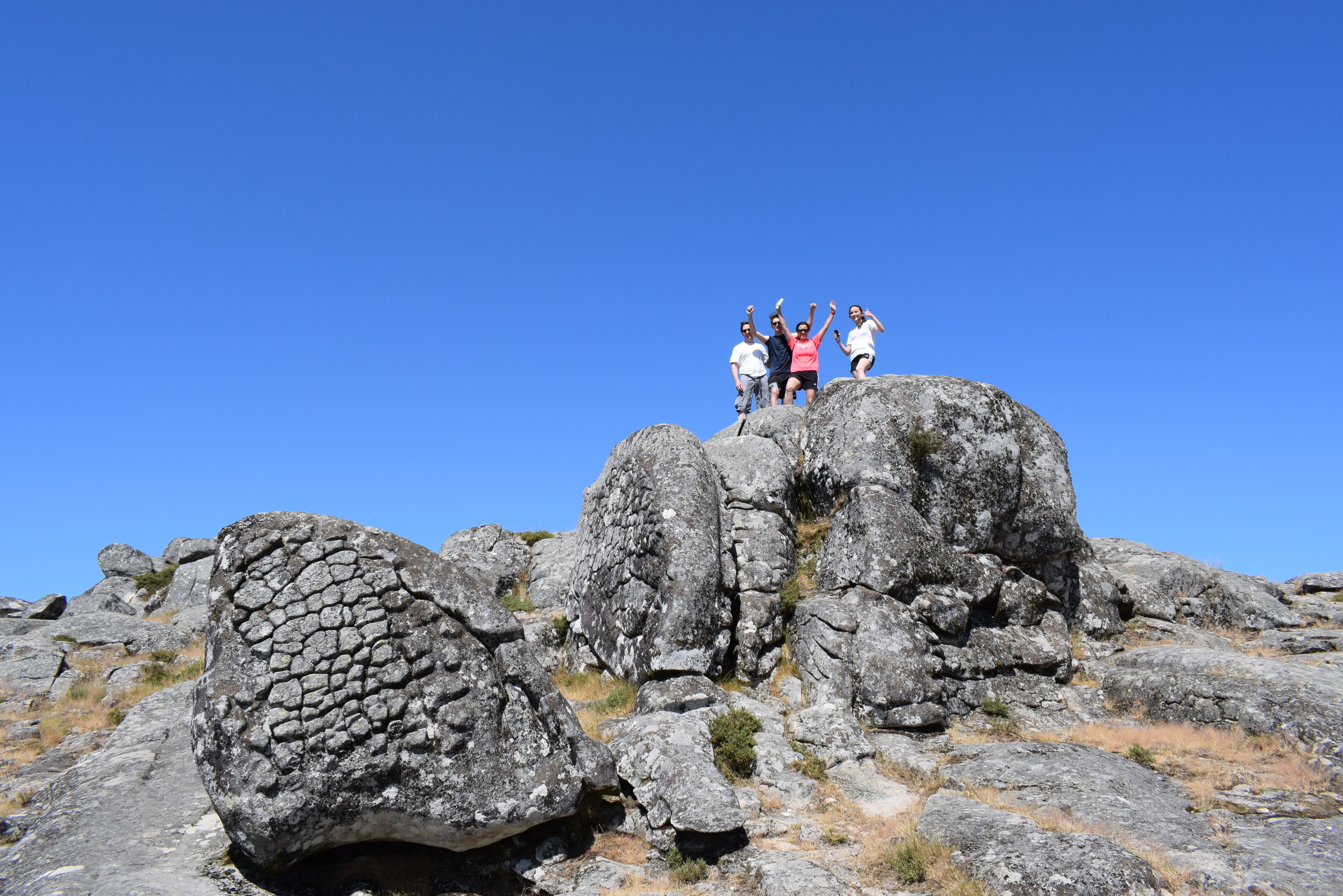 A group of people standing on a rocky outcrop with a clear blue sky in the background.