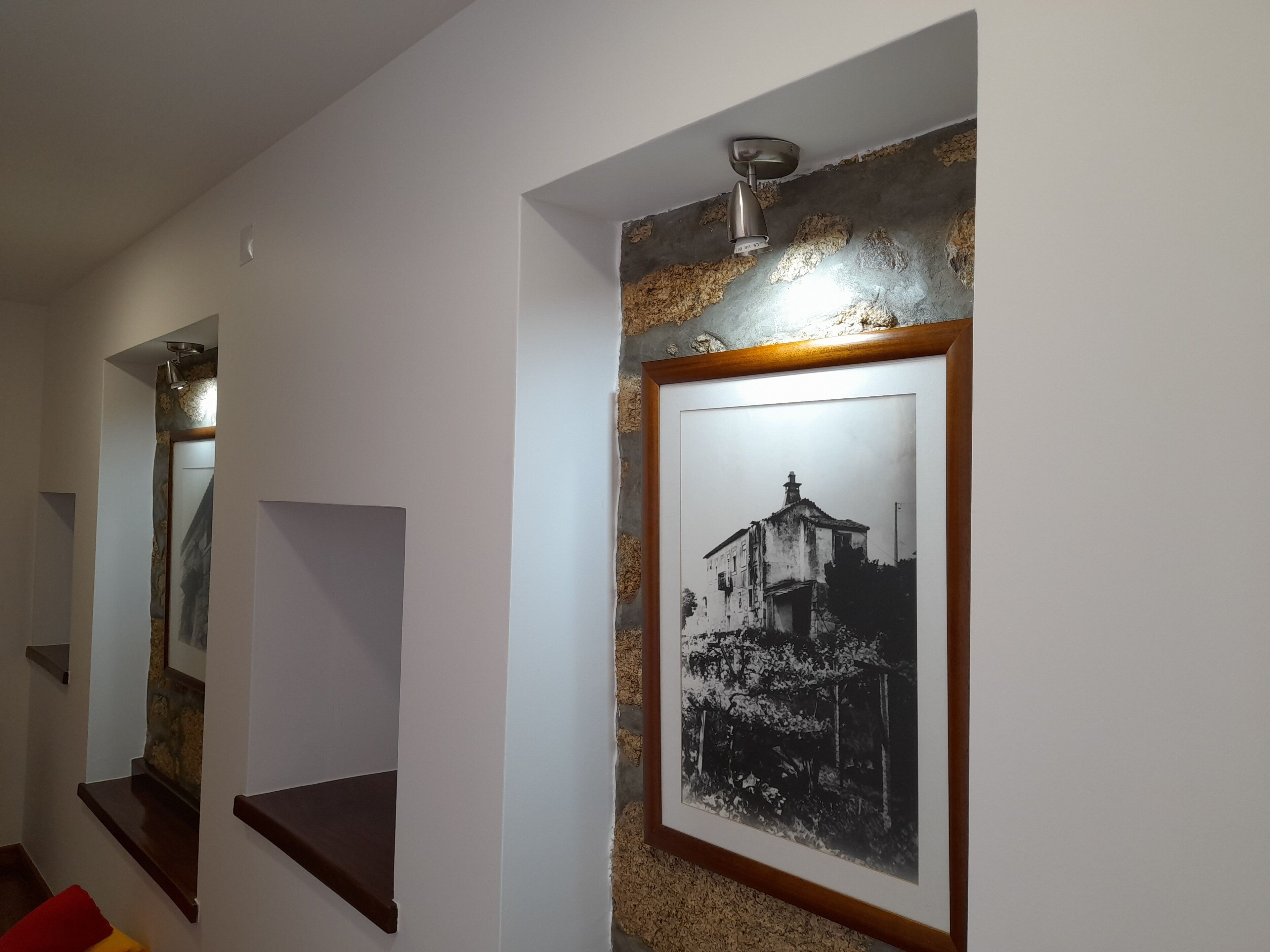 A hallway with a framed black and white photograph on the wall, a small shelf, and a light fixture.