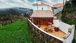 A house with a stone retaining wall, a wooden deck, and a tiled patio.