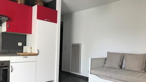 A modern kitchen with red and white cabinets, a built-in oven, and a white refrigerator. There is a beige sofa with a round coffee table in the living area. - Appartement Avec Terrasse et Parking à Anglet (Anglet)