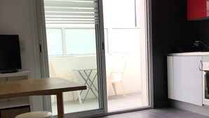 A modern kitchen with a red cabinet, a dining area with a table and chairs, and a sliding glass door leading to a balcony. - Appartement Avec Terrasse et Parking à Anglet (Anglet)