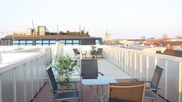 Una terraza en la azotea con mobiliario exterior, una planta en maceta y vistas de la ciudad.