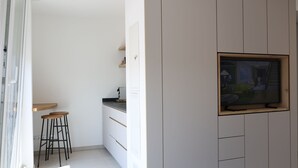 Una cocina moderna con armarios blancos, encimera de madera y televisor integrado. Hay dos taburetes y una ventana con vistas al exterior.