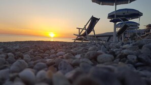 Ein Strand mit Kieselsteinen, einem Sonnenuntergang und zwei Liegestühlen.