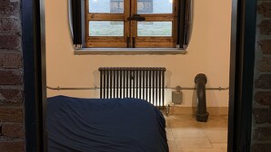 Quarto com uma cama, radiador e janela com parede de tijolos lá fora.