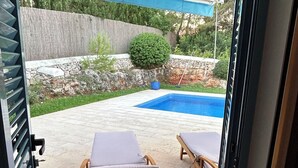 Een overdekt terras met twee houten loungestoelen en een klein zwembad.