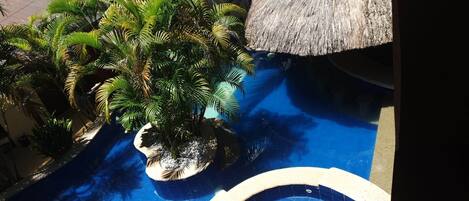 A pool area with palm trees and a thatched roof structure.