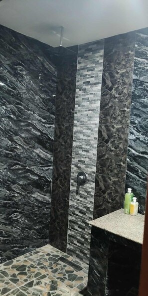 A shower with dark, textured walls and a stone-patterned floor. - Alona Beach Poolside Hotel (Panglao)