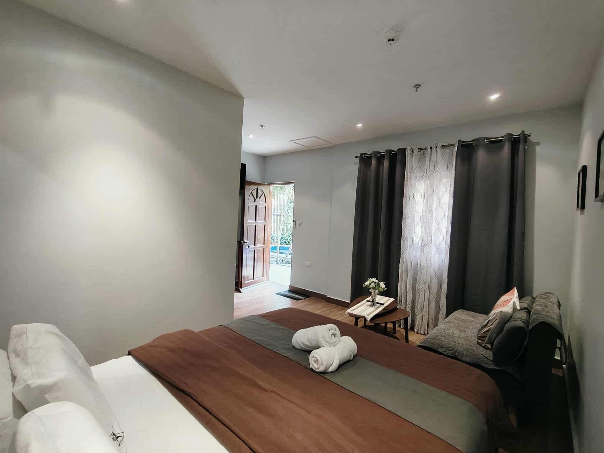 A modern bedroom with a large bed, a small table with a vase, and a view of the outside.