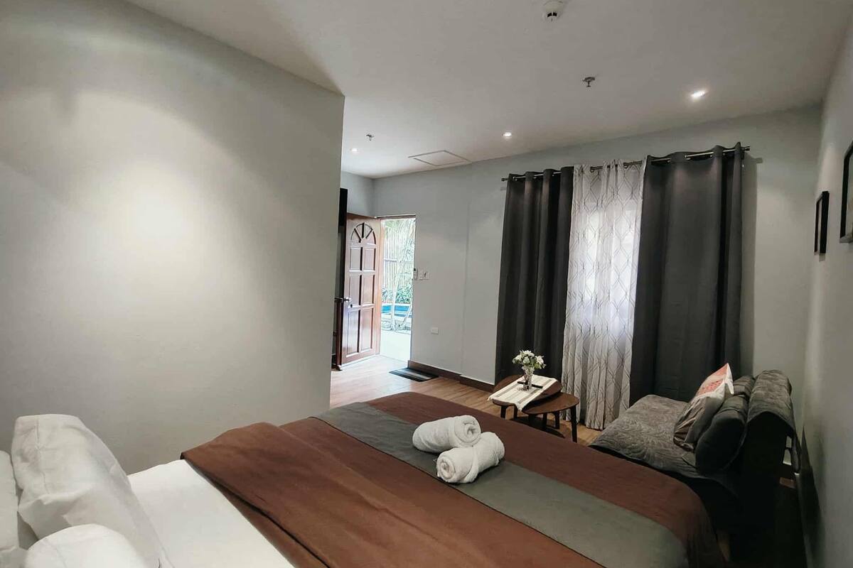 Ein modernes Schlafzimmer mit einem großen Bett, einem kleinen Tisch mit einer Vase und Blick ins Freie.