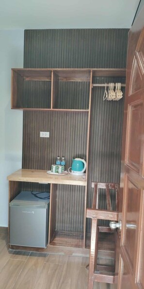 A compact room with a built-in wooden shelf unit, a small table with a blue bowl, and a chair. - Alona Beach Poolside Hotel (Panglao)