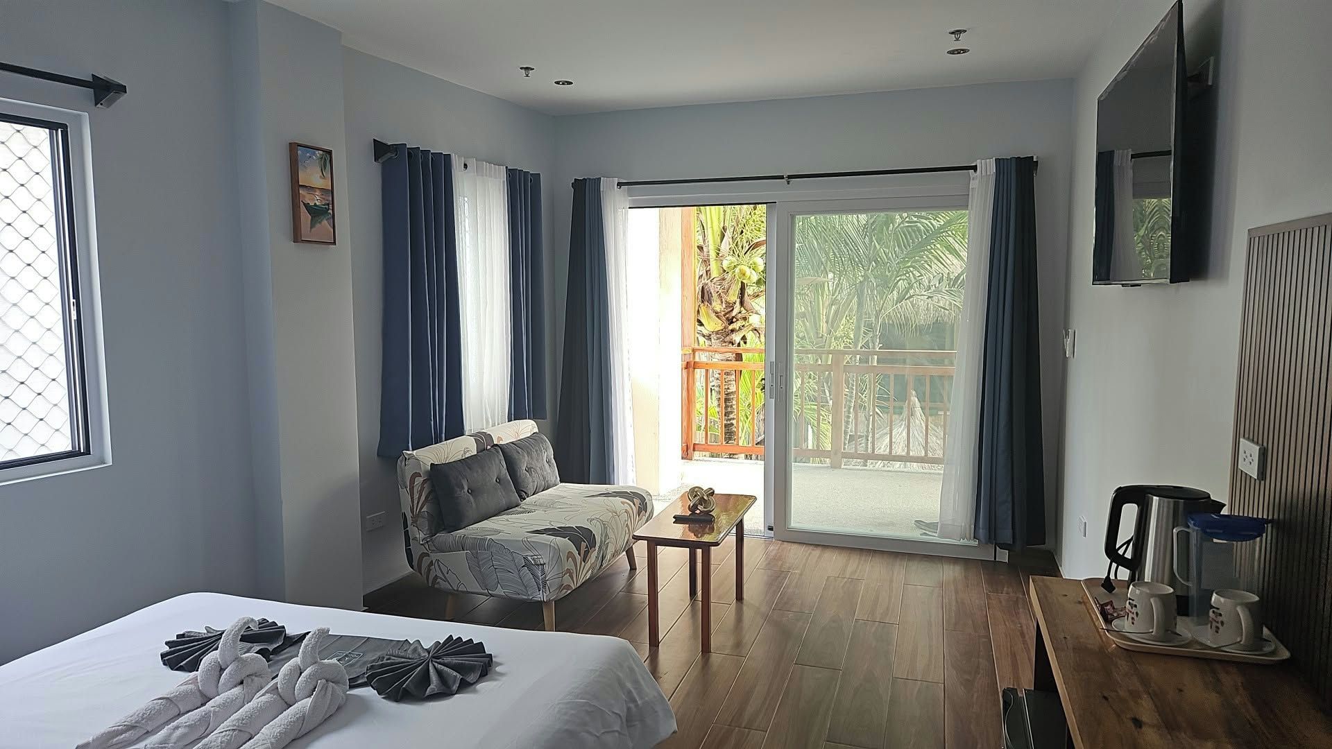 Une chambre d’hôtel avec un lit, un canapé, une petite table et un balcon donnant sur des palmiers.