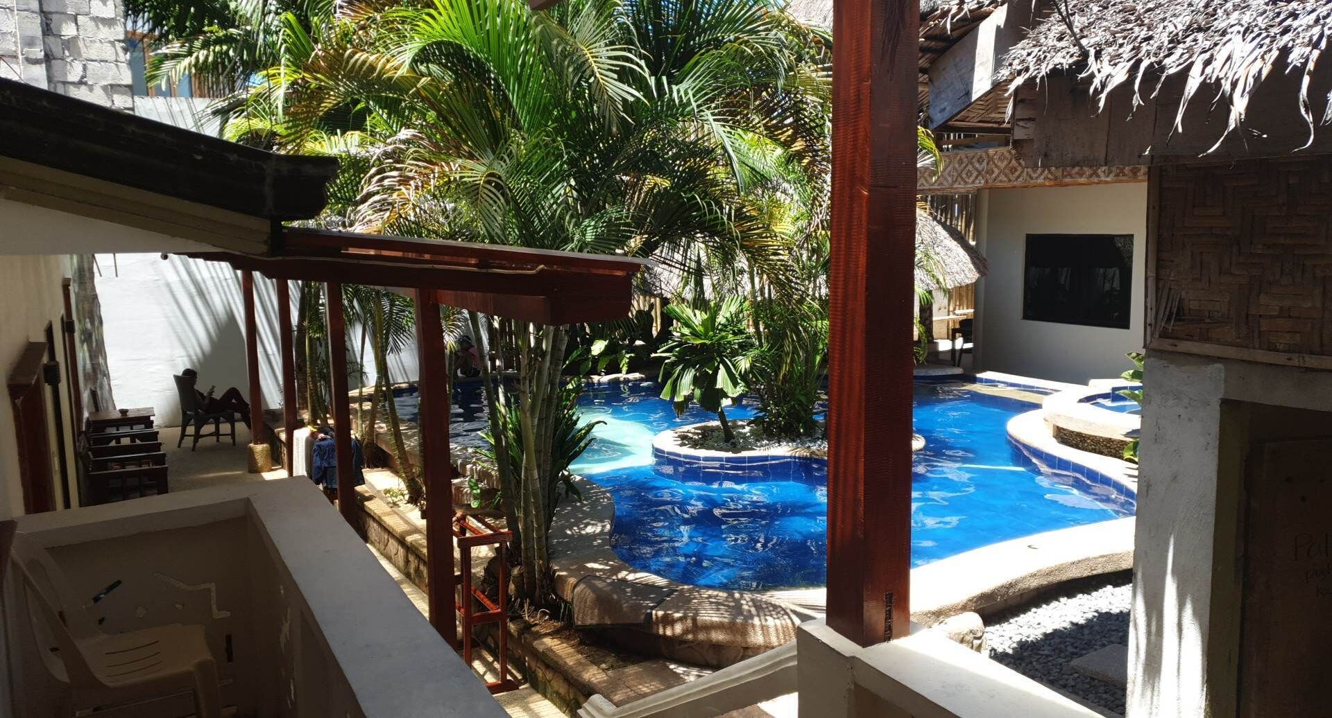 Un espace piscine agrémenté d’une structure à toit de chaume, entouré d’une végétation luxuriante et de palmiers.