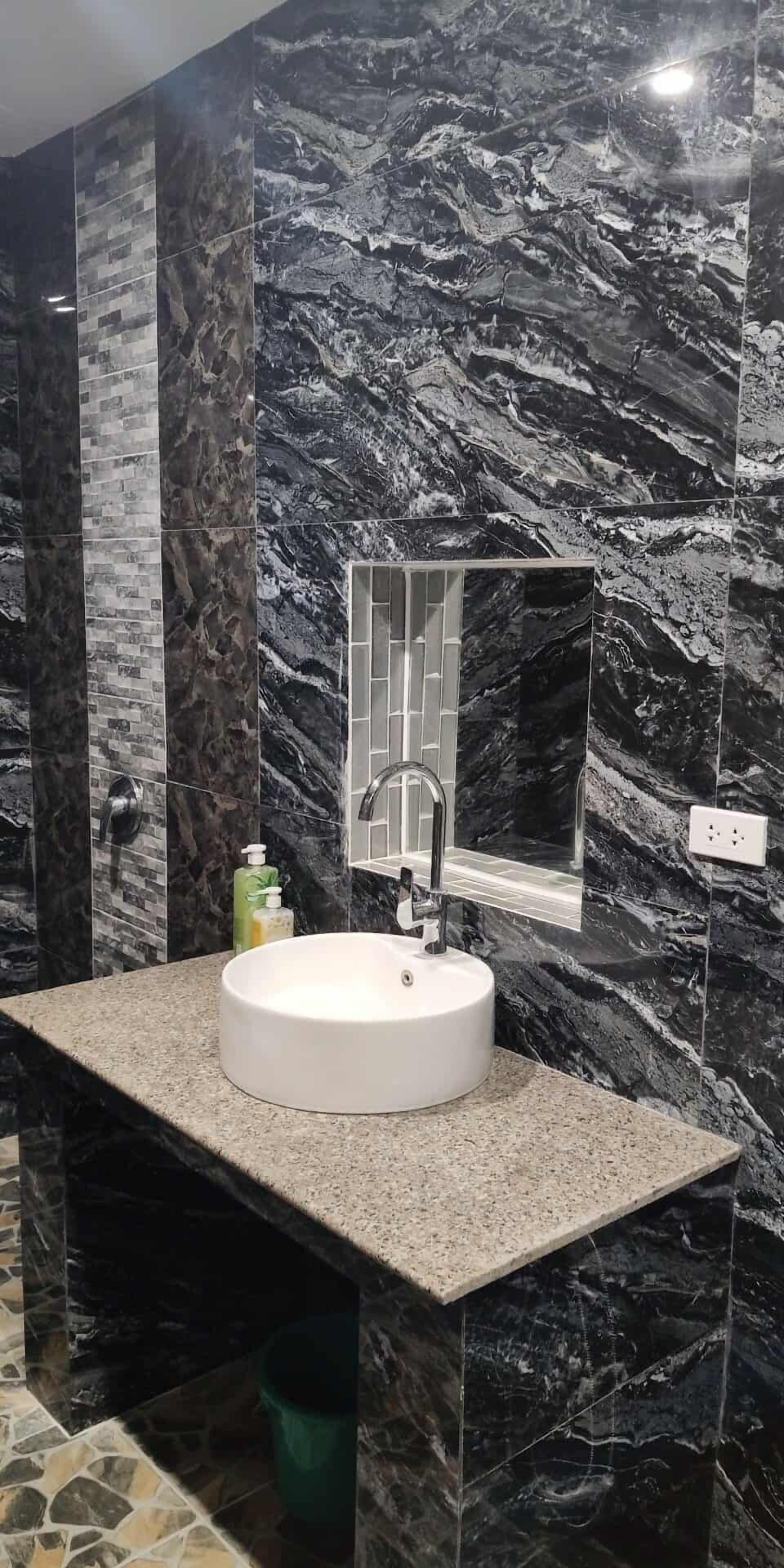 Un baño con un lavamanos blanco, un espejo y paredes de mármol negro.