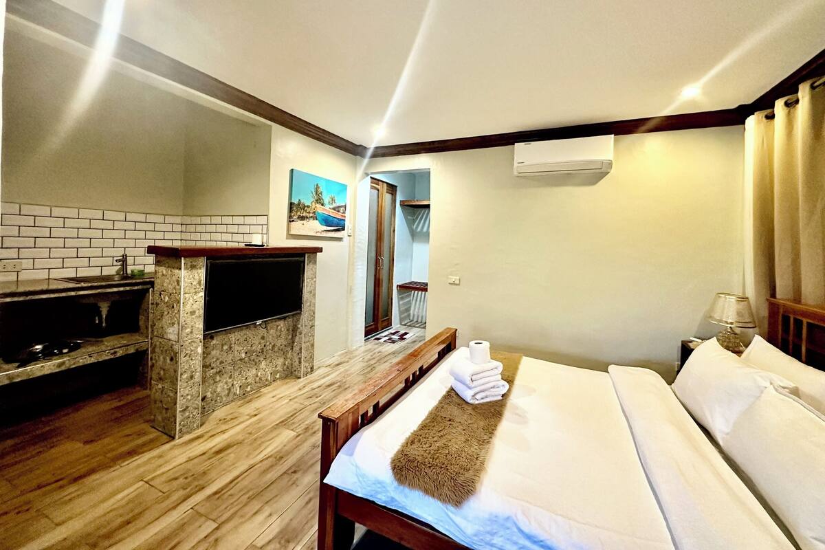 A hotel room with a wooden floor, a bed with white linens, a small table with a lamp, and a brick fireplace.